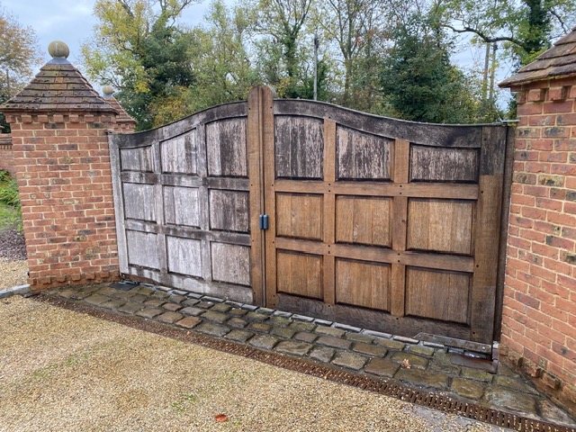 Timber entrance gates between brick piers, with the gravel and setts alongside them cleared and swept back to a clean edge.
